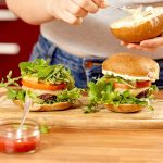 person holding burger with lettuce and tomato